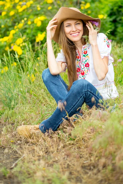 Happy woman sitting on rural road with yellow roses background — Stock Photo, Image