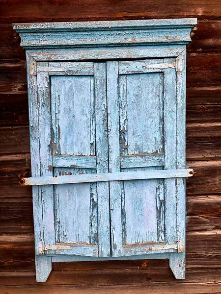 Vieille fenêtre fermée en bois, volets avec peeling vieille peinture bleue, dans une vieille maison en bois faite de rondins, bois naturel. — Photo