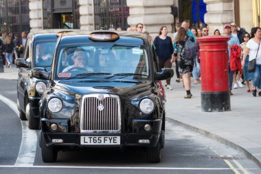 London, England - July 5, 2016: Typical black London cab in central London with United kingdom flags in the background