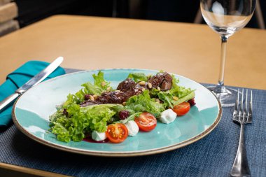 Tavuklu sıcak salata, fırında balkabağı, kiraz domatesleri ve ahşap masadaki seramik tabakta salata karışımı. Seçici odak