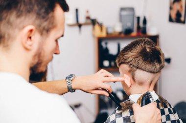 Genç berber, kuaförde küçük şirin bir çocuğun saçını kesiyor.