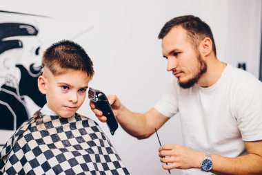 Genç berber, kuaförde küçük şirin bir çocuğun saçını kesiyor.