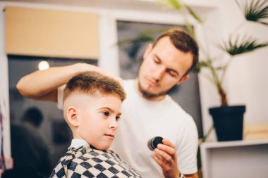 Genç berber, kuaförde küçük şirin bir çocuğun saçını kesiyor.