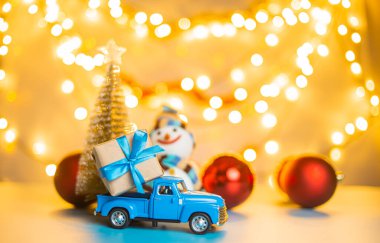 Noel 'i ya da yeni yılı kutlayan arka planda aydınlatılmış ağacı getiren mavi oyuncak araba.