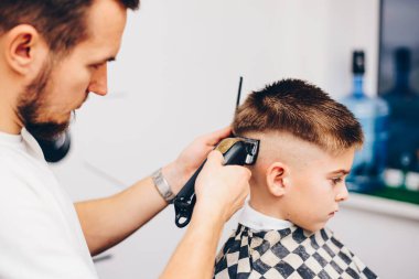 Genç berber, kuaförde küçük şirin bir çocuğun saçını kesiyor.