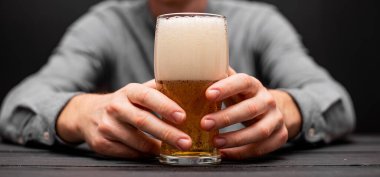 Elinde bira bardağı tutan bir adam var..