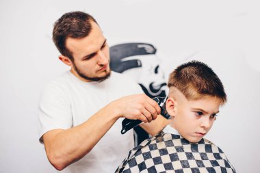 Genç berber, kuaförde küçük şirin bir çocuğun saçını kesiyor.