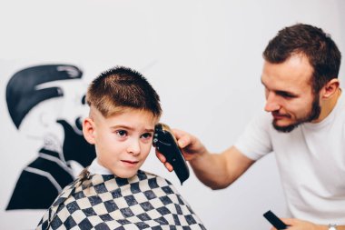 Genç berber, kuaförde küçük şirin bir çocuğun saçını kesiyor.