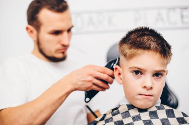 Genç berber, kuaförde küçük şirin bir çocuğun saçını kesiyor.