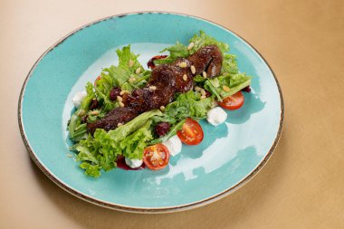 Tavuklu sıcak salata, fırında balkabağı, kiraz domatesleri ve ahşap masadaki seramik tabakta salata karışımı. Seçici odak