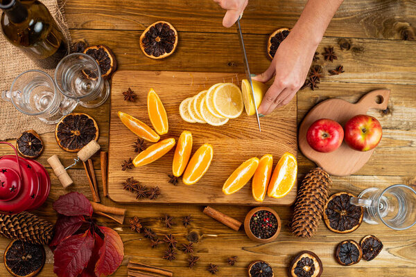 Woman hands slicing orange, cutting citrus fruits. Knife, wooden cutting board, juice squeezer, closeup. Making homemade lemonade