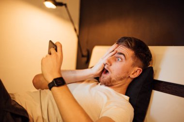 Adam yatakta dinleniyor, akıllı telefon kullanıyor.