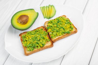 Beyaz ahşap arka planda avokadolu tostlar.