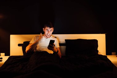 Genç adam yatakta, akıllı telefon kullanıyor.