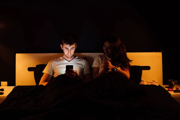 young couple with smartphone in bed at night