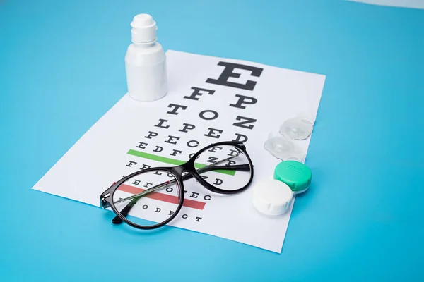 glasses and contact lenses in containers, on snellen eye chart background