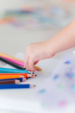Bir çocuğun küçük eli neşeli bir şekilde renkli bir masadan renkli boya kalemleri seçer, yaratıcı sanat projeleri için idealdir.