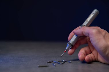 Kırmızı ve turuncu saplı bir tornavida beyaz arka planda şeffaf cam kapaklı bir kutunun içindeki tornavida parçalarının yanında.