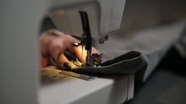 Dikiş işyerindeki profesyonel üretim makinesine beyaz kumaş diken kırpık kadın ellerini kapatın. Elbise üretimi için tekstil tutan terziler. Bulanık arkaplan