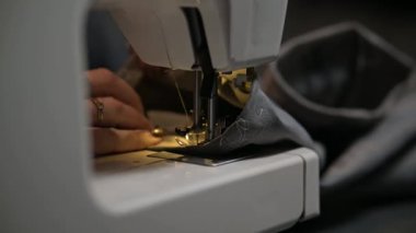 Dikiş işyerindeki profesyonel üretim makinesine beyaz kumaş diken kırpık kadın ellerini kapatın. Elbise üretimi için tekstil tutan terziler. Bulanık arkaplan