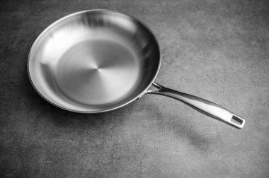 Dökümlü tezgahta paslanmaz çelik kızartma tavası, yalıtılmış minimalist kompozisyon fırçalanmış bitiş ve ergonomik tutuş, dramatik yüksek kontrast