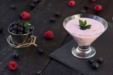 Bir bardak taze çilekli ve yaban mersinli milkshake, smoothie ve pembe, siyah ve ahşap arka planda taze çilek. Sağlıklı yiyecek ve içecek konsepti