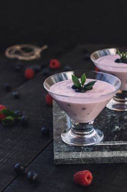 Bir bardak taze çilekli ve yaban mersinli milkshake, smoothie ve pembe, siyah ve ahşap arka planda taze çilek. Sağlıklı yiyecek ve içecek konsepti