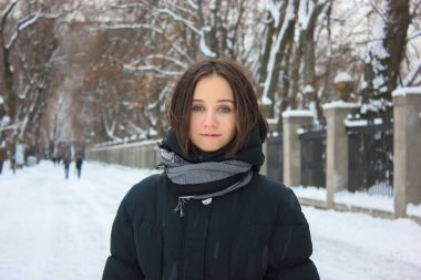 Basit kısa saçlı, siyah montlu ve fularlı mutlu bir esmer. Öğleden sonra kar kaplı bir kış parkında gülümseyen Ukraynalı kız. Kiev, Avrupa.