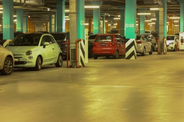 Well-lit parking with easy navigation in the mall with many cars in the evening, gray concrete road for traffic and separating numbered poles 