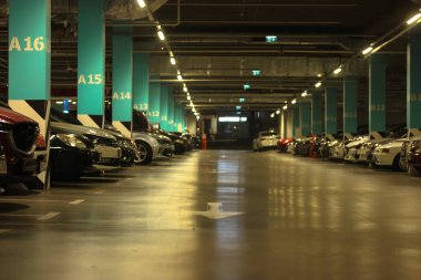 Well-lit parking with easy navigation in the mall with many cars in the evening, gray concrete road for traffic and separating numbered poles 