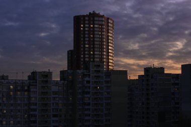 Uzun kırmızı tuğla bina ve arkasındaki birçok ev akşam üzeri mor turuncu bir gökyüzünün arka planına karşı. Modern mimari Kiev, Ukrayna