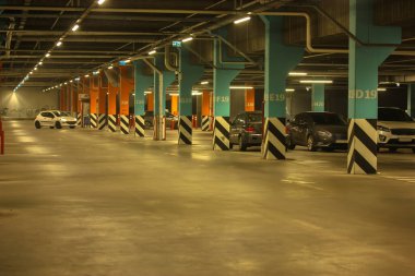 Well-lit parking with easy navigation in the mall with many cars in the evening, gray concrete road for traffic and separating numbered poles 