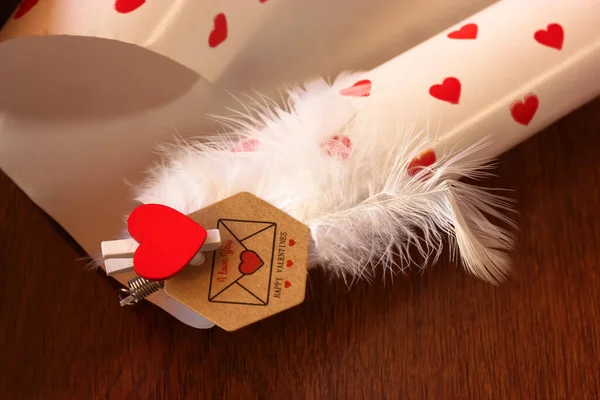 Brown envelope with a note of love confession for a loved one on Valentine\'s Day, the inscription I love you and a red heart with white feathers.