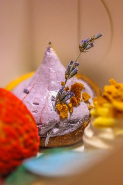 Masanın üzerinde mor lavanta çiçeğiyle süslenmiş maskara peynirli farklı renkli meyveli kekler. Fransa 'da bir kafe.