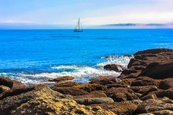 Veleiro branco em nevoeiro no horizonte e pedras maciças em primeiro plano, Oceano Atlântico no verão, Cantábria, Santander, Espanha — Fotografia de Stock