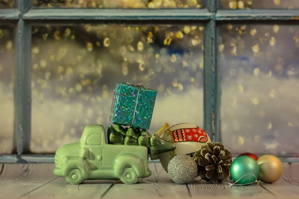 Carro de brinquedo com uma árvore de Natal e uma caixa de presentes no telhado contra a janela — Fotografia de Stock