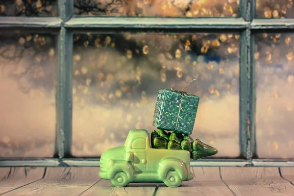 Spielzeugauto mit Weihnachtsbaum und Geschenkkiste auf dem Dach gegen das Fenster — Stockfoto