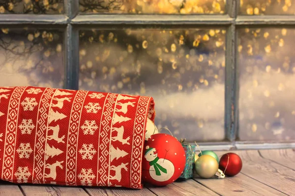 Round Christmas tree toys, and a toy with a snowman image, fell out of a red bag with gifts from Santa Claus on a wooden table. New Years Eve background