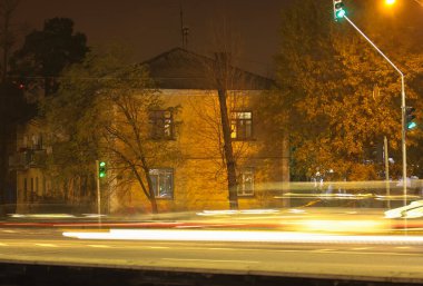 Kyiv 'deki iki katlı ev ve akşamları otoyolda giden arabaların bulanık ışıkları. Yeşil trafik ışığı.