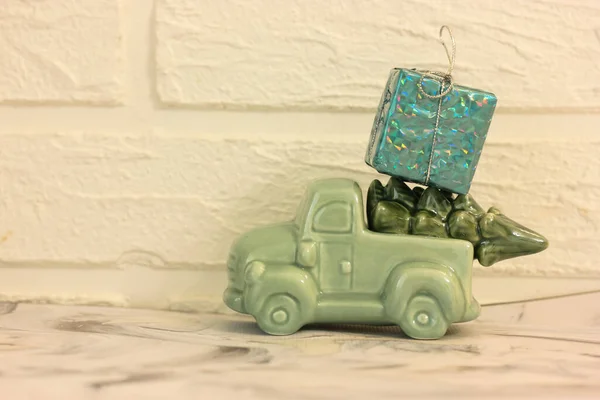 Ein Spielzeugauto trägt einen Weihnachtsbaum mit Neujahrsgeschenken, eine blaue Schachtel mit Geschenken und eine silberne Schleife auf dem Dach. — Stockfoto
