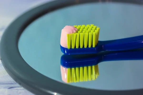Blaue Zahnbürste mit grünen Borsten in Großaufnahme, die sich im Spiegel spiegelt, rosa Zahnpasta. Mundhygiene und Zahnpflegeprodukte für den Alltag — Stockfoto