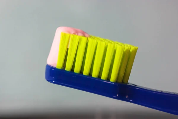 Escova de dentes azul com cerdas verdes close-up, pasta de dentes rosa. Produtos de higiene e cuidados dentários do dentista — Fotografia de Stock