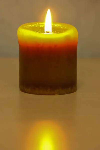 Burning yellow candle on a wooden surface close-up against a blue wall in the interior. Minimalism and no people — Stock Photo, Image