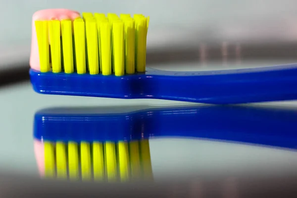 Blue toothbrush with green bristles close-up reflected in mirror, pink toothpaste. Oral hygiene and dental care products for the daily routine — Stock Photo, Image