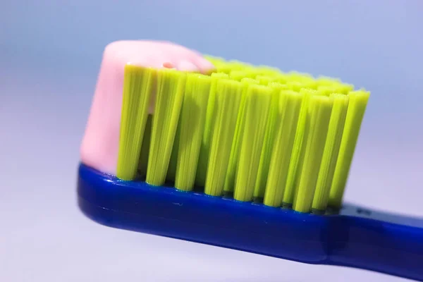 Escova de dentes azul com cerdas verdes close-up, pasta de dentes rosa. Produtos de higiene e cuidados dentários do dentista — Fotografia de Stock