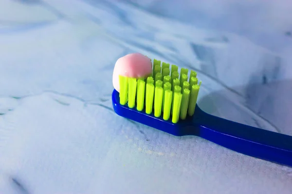 Blue toothbrush with green bristles close-up, pink toothpaste. Dental hygiene and care products from the dentist — Stock Photo, Image