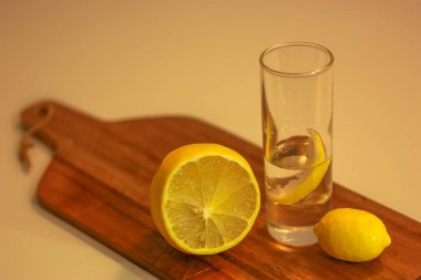 Bardakta votka ya da cin, bir dilim limon dilimi ve tahta kesme tahtasının üzerinde limon dilimi. Kırmızı arkaplan