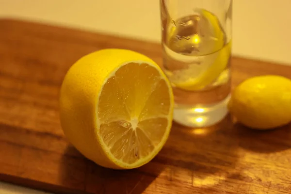 Wodka oder Gin in einem Schnapsglas mit einer Scheibe Zitrone und einer halbierten Zitrone auf einem Holzschneidebrett. Roter Hintergrund — Stockfoto