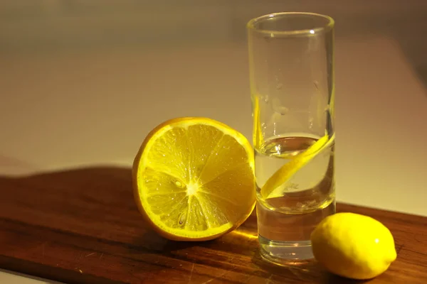 Wodka oder Gin in einem Schnapsglas mit einer Scheibe Zitrone und einer halbierten Zitrone auf einem Holzschneidebrett. Roter Hintergrund — Stockfoto