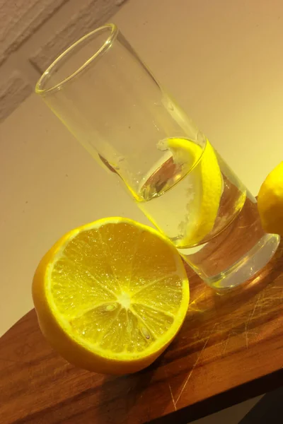 Wodka oder Gin in einem Schnapsglas mit einer Scheibe Zitrone und einer halbierten Zitrone auf einem Holzschneidebrett. Roter Hintergrund — Stockfoto